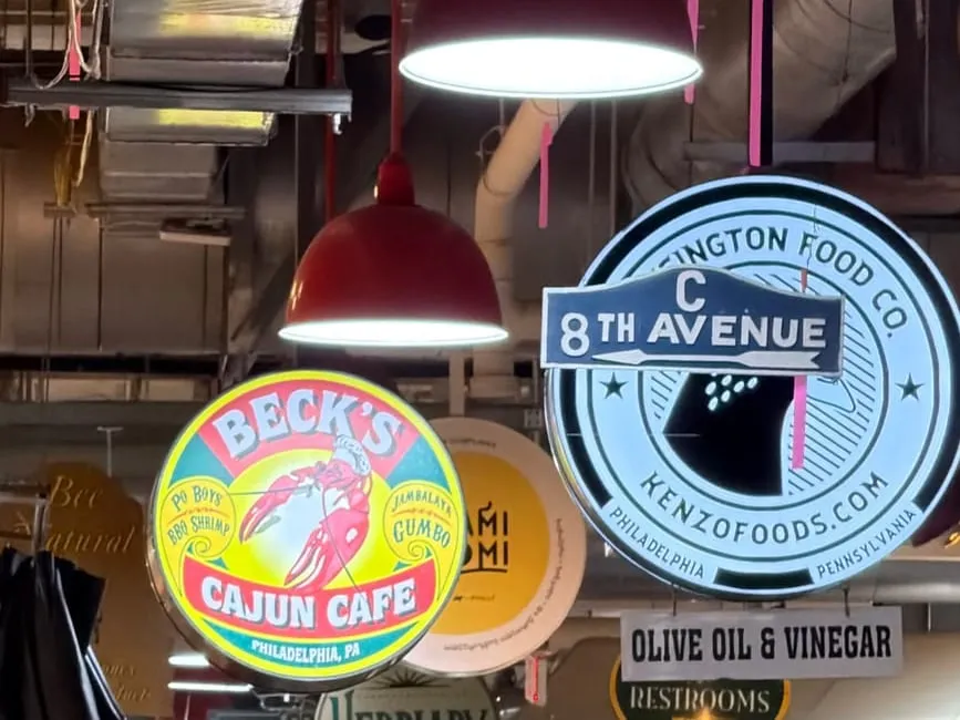 The Beck's Cajun Cafe sign hanging among the signs and red lamps of Reading Terminal Market