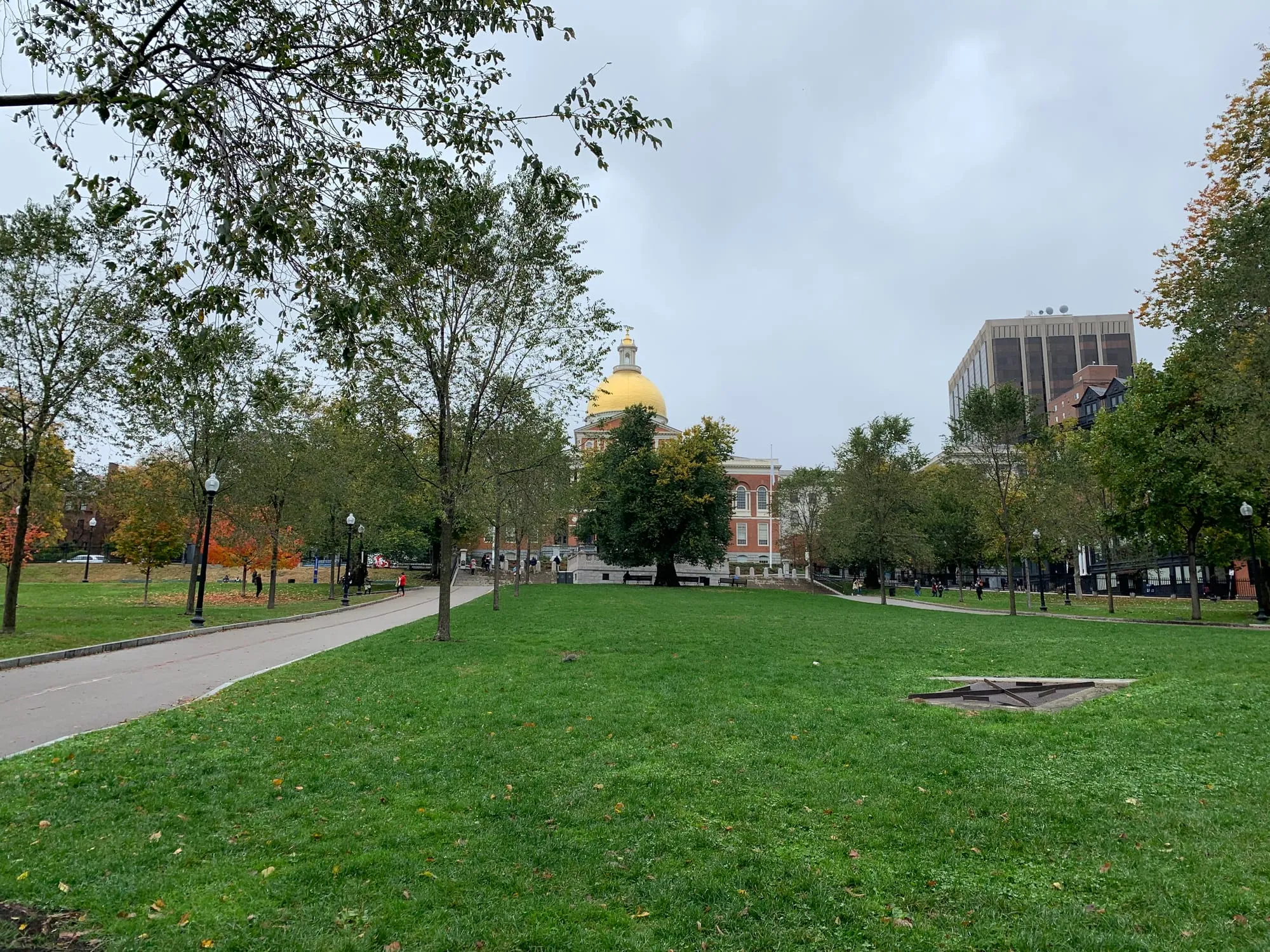 Green lawns and trees on Boston Common, with the State House's gold dome beyond