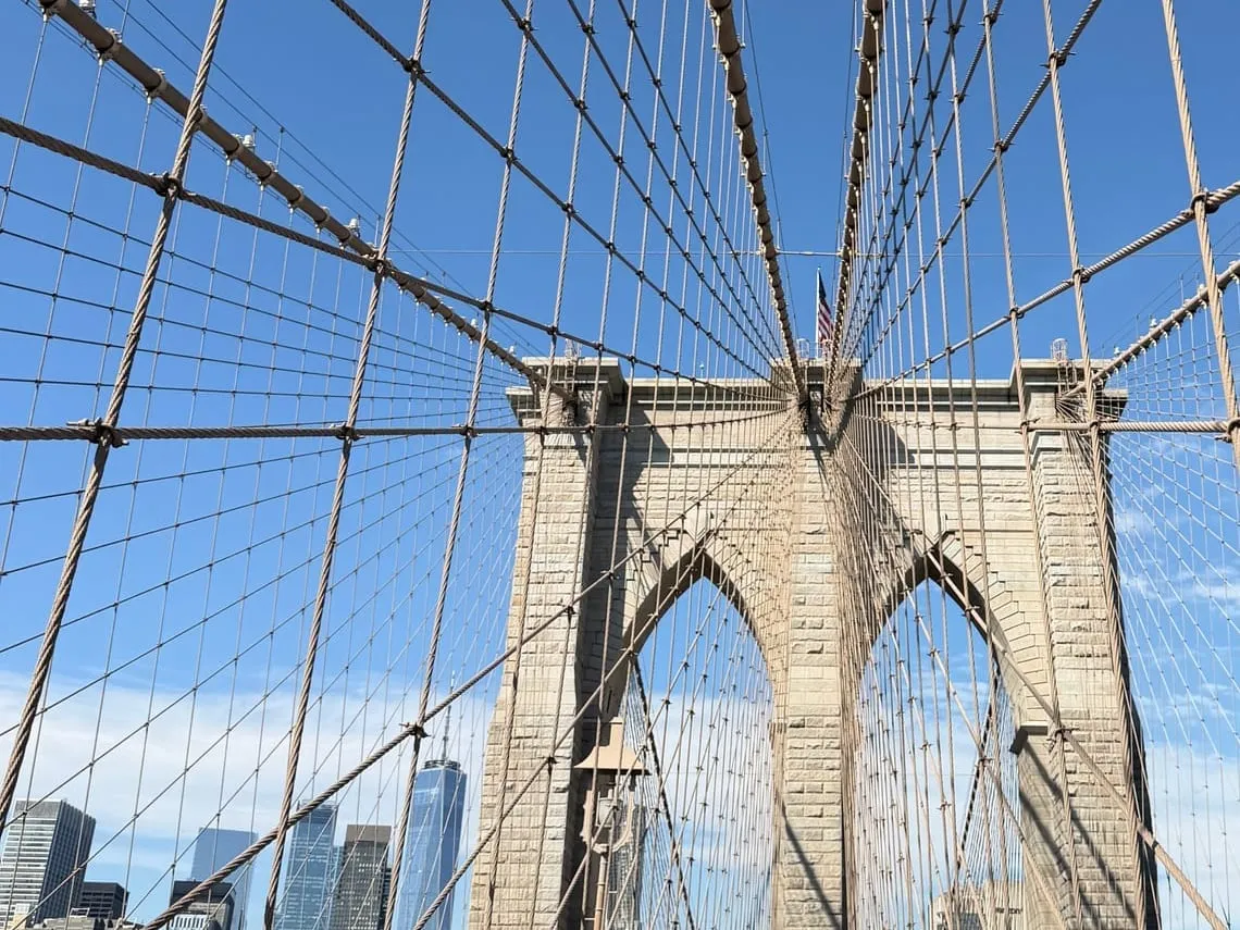 The Brooklyn Bridge's stone tower and web of cables against a bright blue sky
