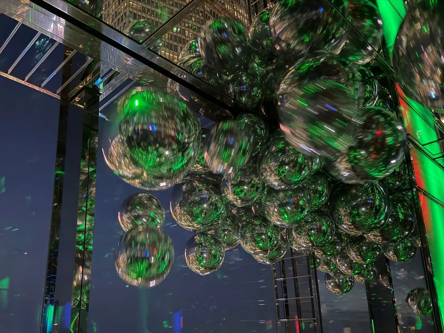 SUMMIT's room of giant mirrored silver balloons, glowing green, above the night skyline